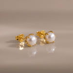 Load image into Gallery viewer, Gold earrings with pearl studs on a beige background