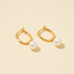 Load image into Gallery viewer, Gold hoop earrings with pearl accents on a beige background