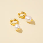 Load image into Gallery viewer, Gold hoop earrings with white pearls on a beige background