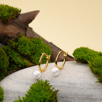 Load image into Gallery viewer, Gold hoop earrings with white pearls on a stone surface with green moss.