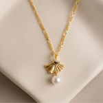 Load image into Gallery viewer, Gold necklace with a fan-shaped pendant and pearl drop on a beige background