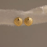 Load image into Gallery viewer, Gold shell-shaped earrings on a beige fabric background