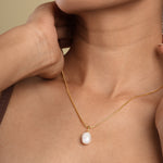 Load image into Gallery viewer, A close-up of a woman's neck and chest as she wears a delicate gold snake chain necklace with a single baroque pearl pendant. Her hand gently touches the side of her neck, and she is wearing a brown patterned headscarf.