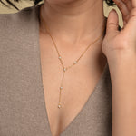 Load image into Gallery viewer, A close-up of a model wearing an elegant gold lariat necklace from Zewory Jewellery. The delicate Y-necklace, featuring five sparkling bezel-set crystals, is showcased resting gracefully against her skin and a neutral-coloured top.