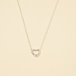 Load image into Gallery viewer, A clean, minimalist product shot of a silver open heart necklace on a neutral cream background. The image clearly displays the delicate chain and the simple, polished open heart pendant, a classic and timeless piece of jewellery.