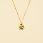 Load image into Gallery viewer, A clean, minimalist product shot of a gold necklace with an organically shaped, bezel-set stone pendant. The image clearly displays the smoky translucent gemstone and delicate gold chain against a neutral cream background.