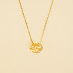 Load image into Gallery viewer, A clean, minimalist product shot of a gold floral necklace on a neutral background. The image highlights the textured petals and single pearl at the center of the flower pendant, showcasing its delicate botanical design.