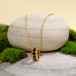 Load image into Gallery viewer, A modern gold honeycomb necklace from Zewory Jewellery, displayed in a serene natural setting. The unique, black-and-crystal-accented barrel pendant is draped over a smooth, light-grey stone and surrounded by fresh green moss.