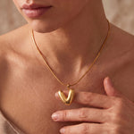 Load image into Gallery viewer, A close-up of a model wearing a delicate gold chain necklace with a polished, rounded V-shaped pendant, with her hand resting near the necklace.