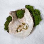 Load image into Gallery viewer, An artistic product shot of modern gold and pearl stud earrings from Zewory Jewellery. The pair of abstract, open-design studs are elegantly displayed inside a large seashell on a bed of white sand and moss.