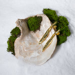 Load image into Gallery viewer, A pair of striking, twisted gold drop statement earrings from Zewory Jewellery, creatively displayed on a large seashell. The product is set on a bed of white sand and accented with vibrant green moss for a natural, luxurious aesthetic.