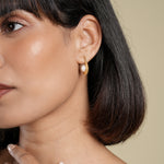 Load image into Gallery viewer, Close-up of a woman wearing a gold earring with a pearl on a beige background