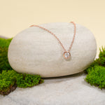 Load image into Gallery viewer, A delicate rose gold solitaire necklace from Zewory Jewellery, displayed in a serene natural setting. The minimalist, bezel-set crystal pendant is draped over a smooth, light-grey stone and surrounded by fresh green moss.