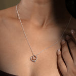 Load image into Gallery viewer, A close-up of a model wearing an elegant two-tone interlocking hearts necklace from Zewory Jewellery. The romantic pendant, featuring a large silver open heart and a smaller rose gold open heart, rests gracefully against her skin.