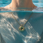 Load image into Gallery viewer, A gold necklace with a double-ring pendant is worn by a model standing in a swimming pool, with water and sunlight reflecting across the chest.