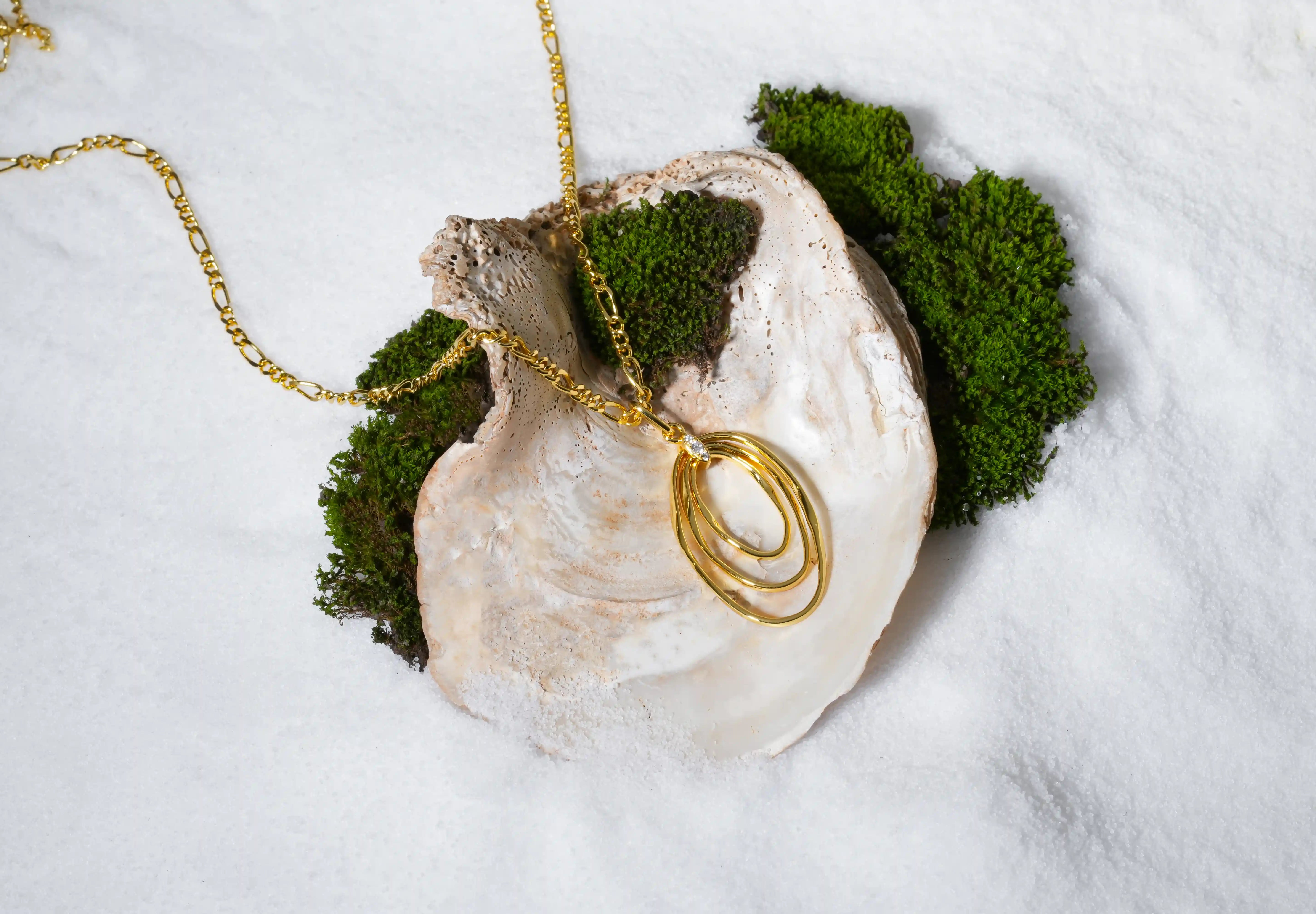 Zewory gold abstract pendant necklace styled on an oyster shell with green moss on marble background.
