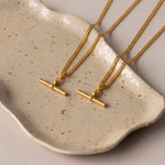 Load image into Gallery viewer, Two gold chain necklaces with minimalist bar pendants resting on a speckled cream ceramic dish.
