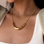 Load image into Gallery viewer, A close-up of a model wearing a polished gold crescent-shaped pendant necklace with a delicate chain, styled with a white ribbed tank top and a light sage green cardigan.
