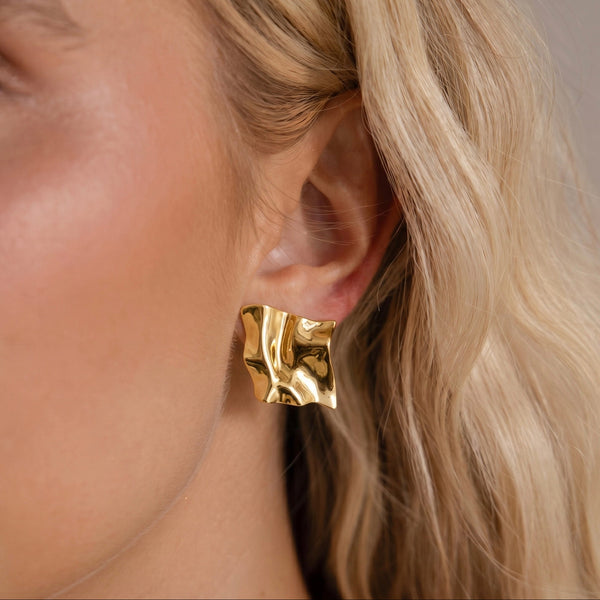 Close-up of a gold earring worn by a person with blonde hair.