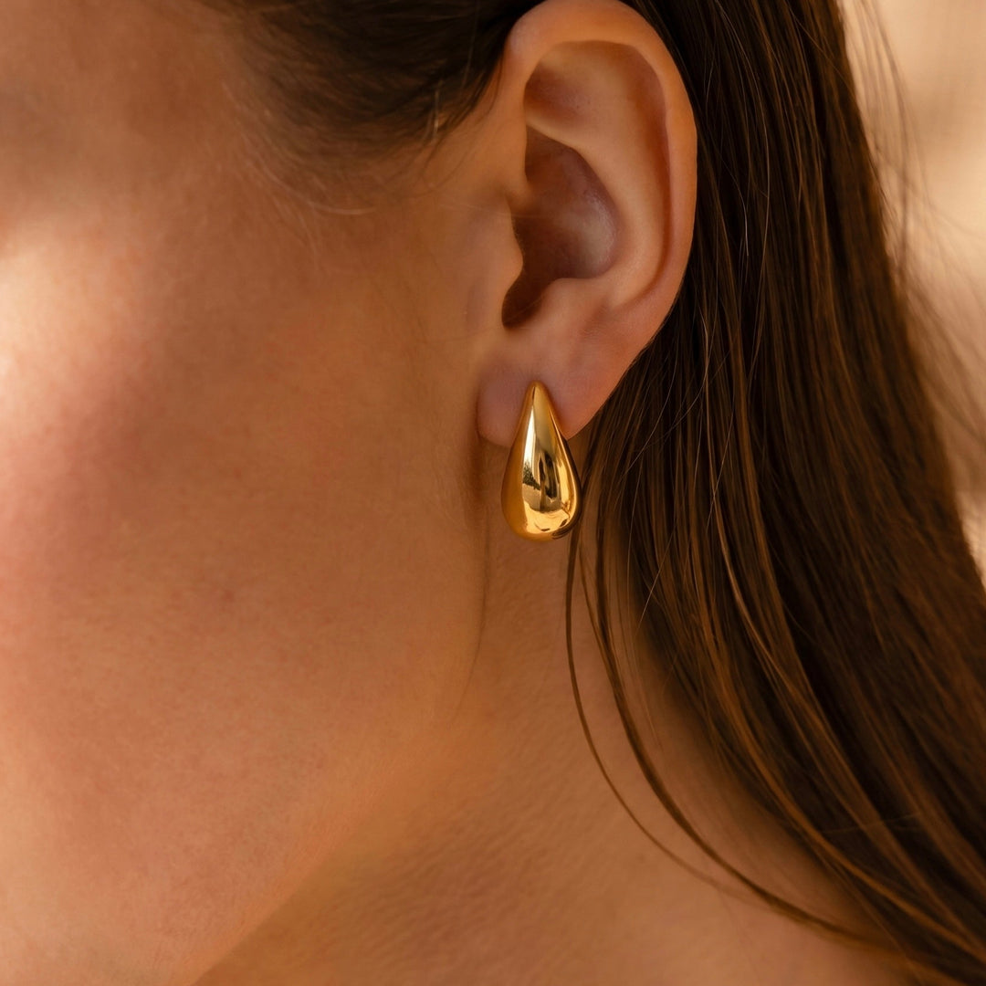 Close-up of a person wearing a gold hoop earring with a blurred background