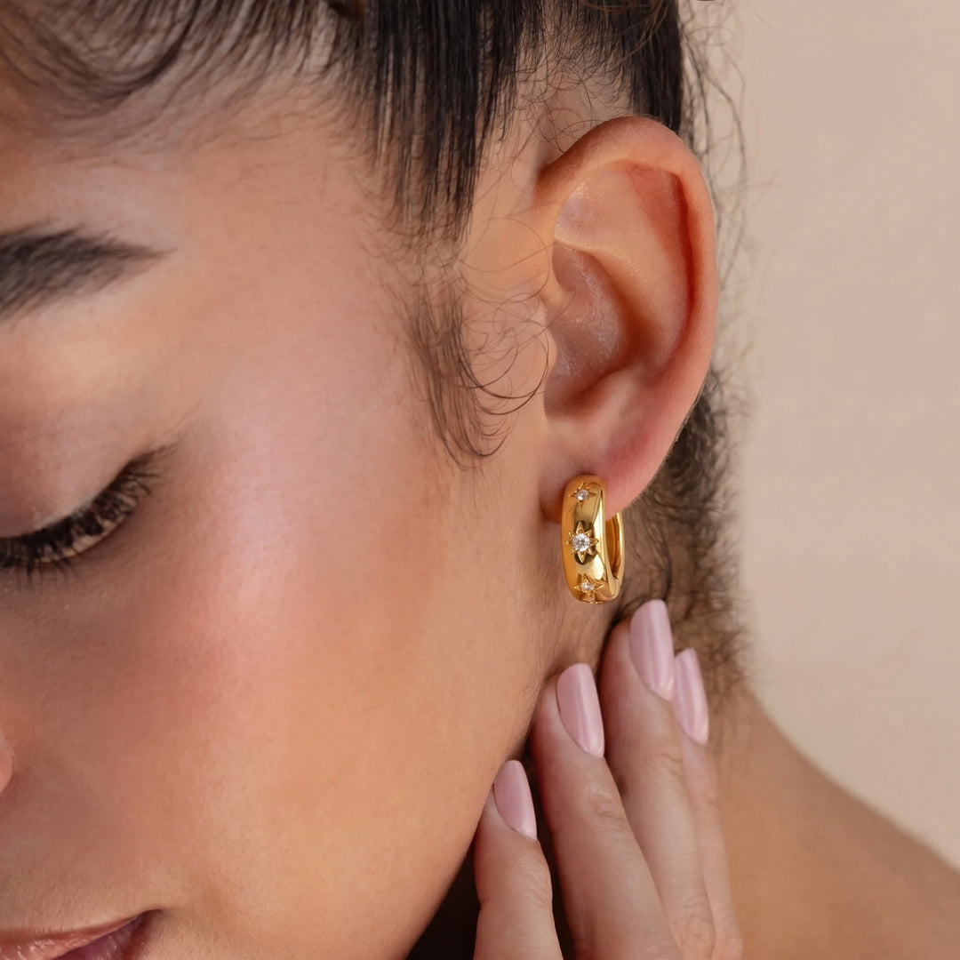 Close-up of a person wearing a gold hoop earring with a neutral background