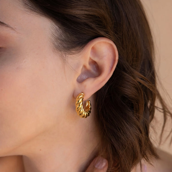 Close up of a person wearing 18K gold plated twist earrings crafted from 925 sterling silver, featuring a polished twisted hoop design.