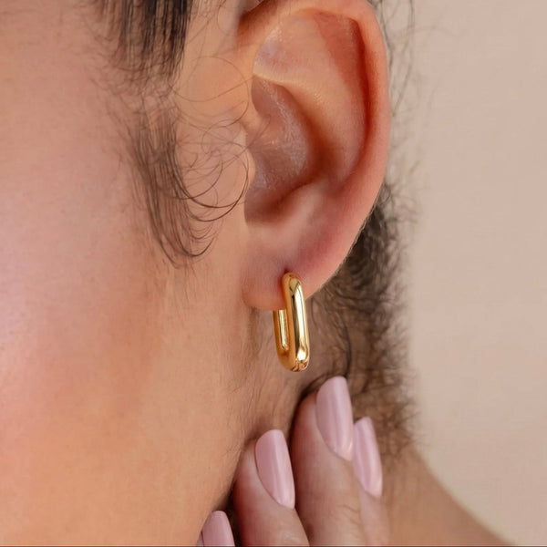 Close-up of a person wearing a gold hoop earring with a neutral background