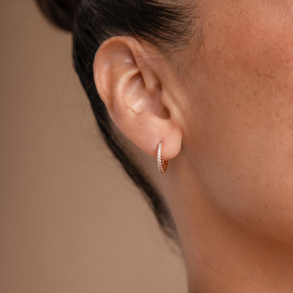 Close-up of an ear wearing a gold hoop earring against a neutral background