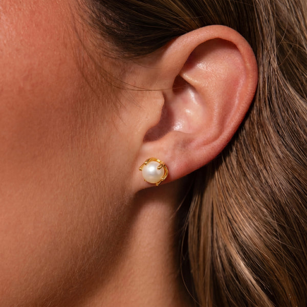 Close-up of an ear wearing a pearl earring with a gold setting.