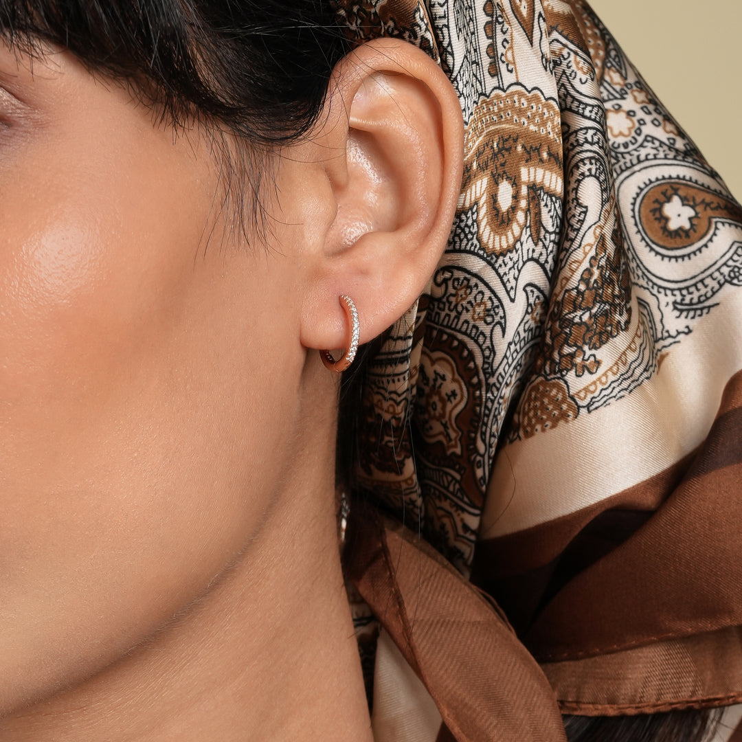 Close-up of an ear with a gold earring, wearing a patterned scarf.