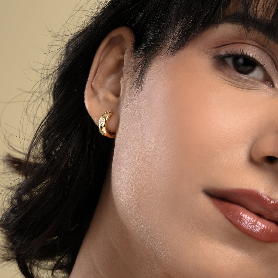 Close-up of a woman wearing a gold earring with a neutral background
