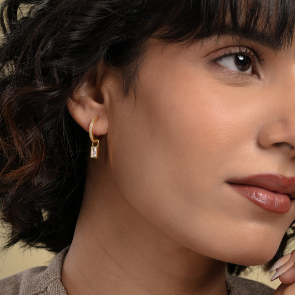 Close-up of a woman wearing gold hoop earrings with a neutral background