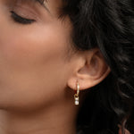 Load image into Gallery viewer, Close-up of a woman wearing gold hoop earrings with a dark background
