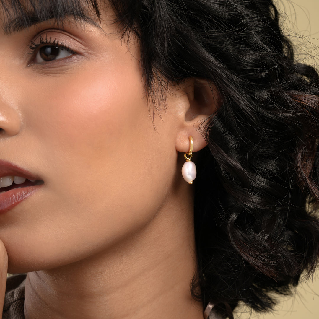 Close-up of a woman wearing gold hoop earrings with pearl-like stones.