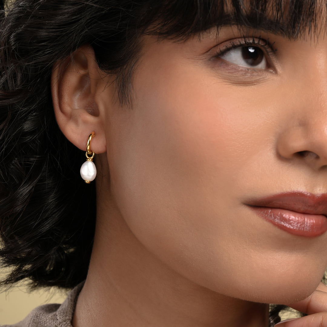 Close-up of a woman wearing pearl earrings with a neutral background