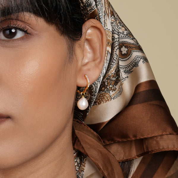 Close-up of an ear wearing a pearl earring with a patterned headscarf.