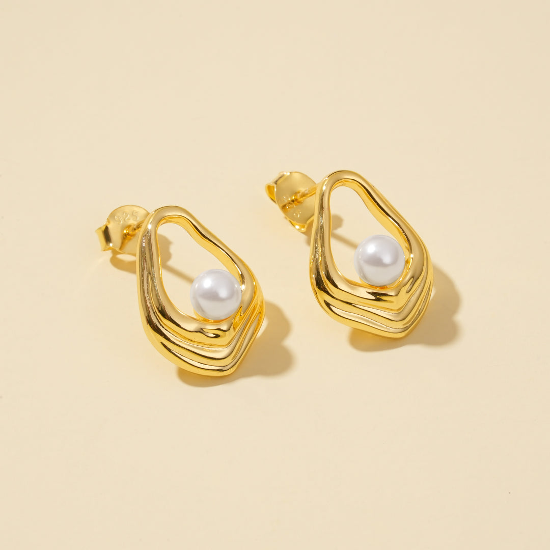 Gold earrings with pearl centers on a beige background