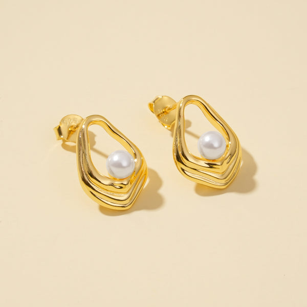 Gold earrings with pearl centers on a beige background