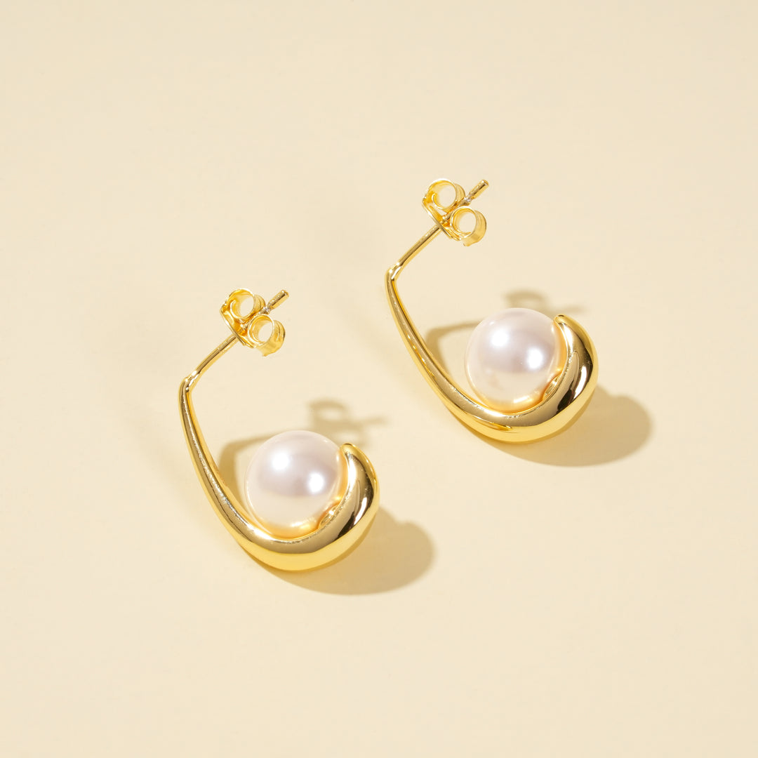 Gold earrings with pearl drops on a beige background