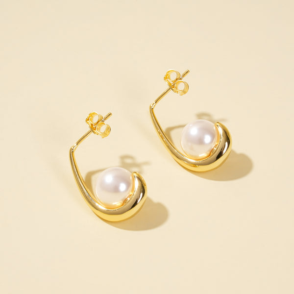 Gold earrings with pearl drops on a beige background