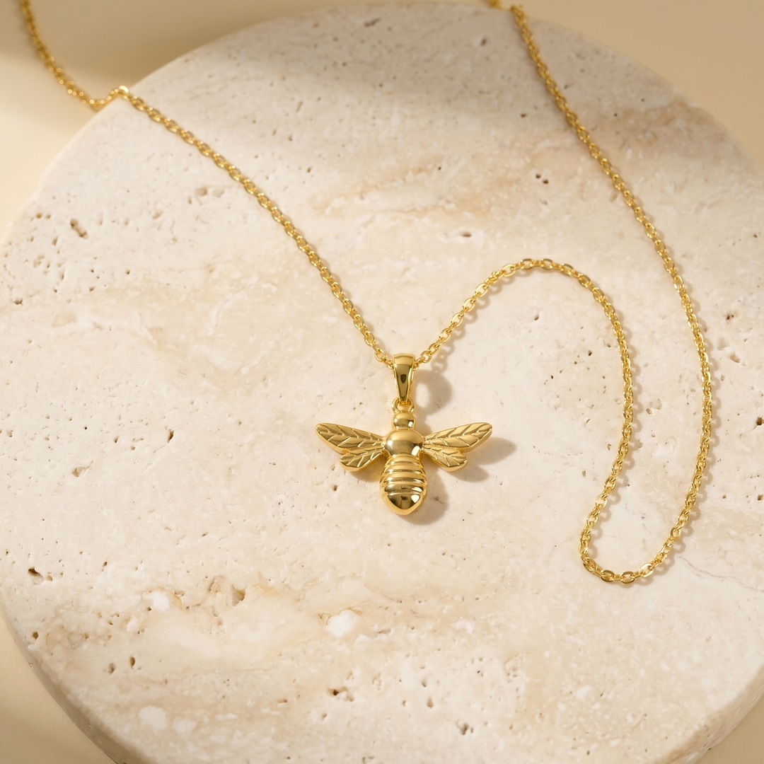 Gold bee necklace on a textured stone surface