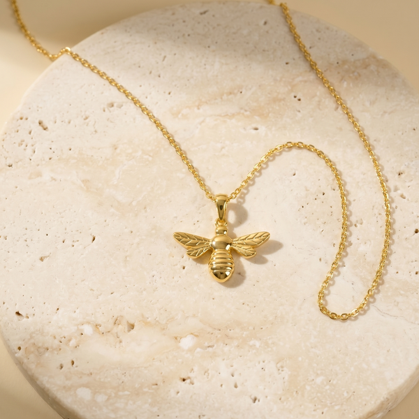 Gold bee necklace on a textured stone surface
