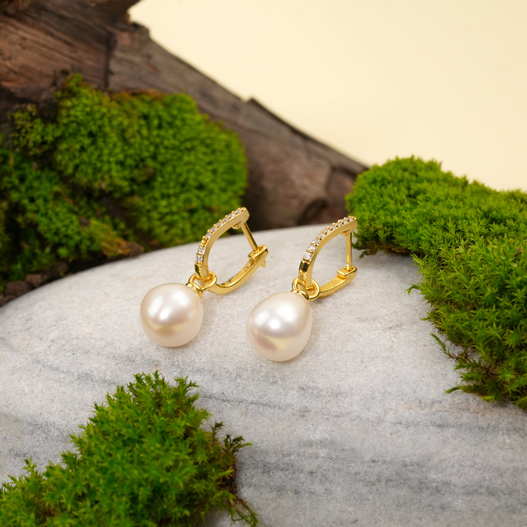 Gold earrings with pearls on a stone surface with green moss