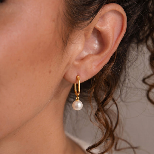 Gold earring with a pearl drop worn by a person