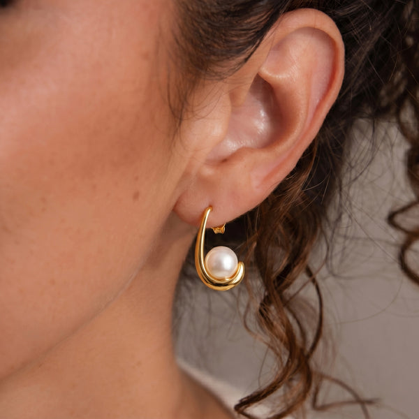 Gold earring with a pearl worn by a person