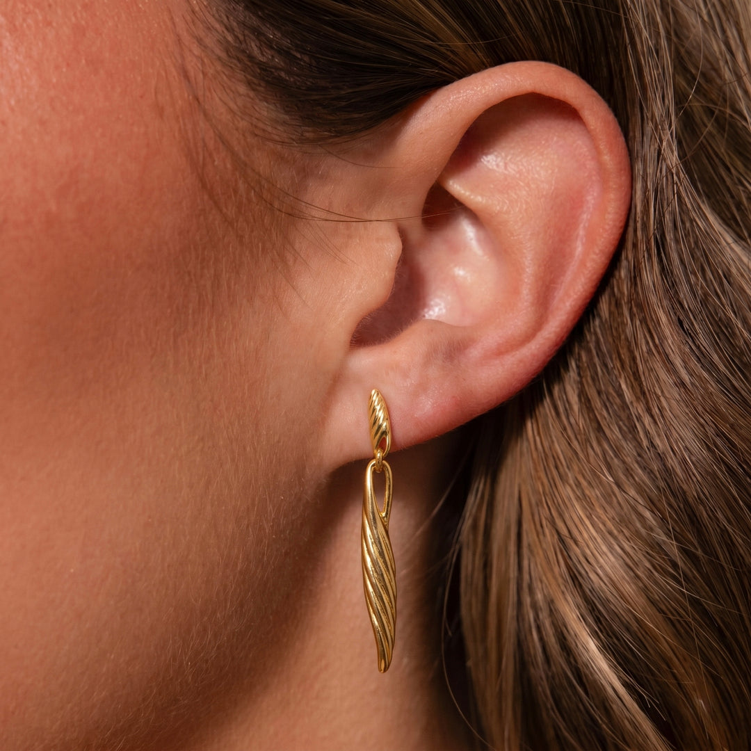 Gold earring worn by a person with brown hair.