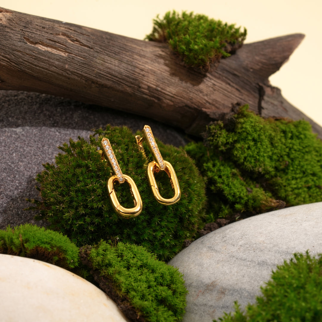 Gold earrings with chain links on a natural background of stones and moss