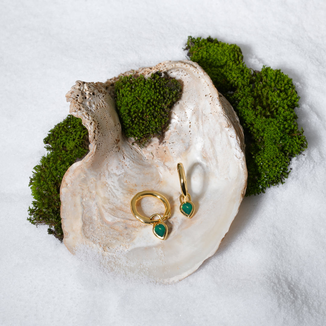 Gold earrings with green gemstones on a white shell surrounded by moss.