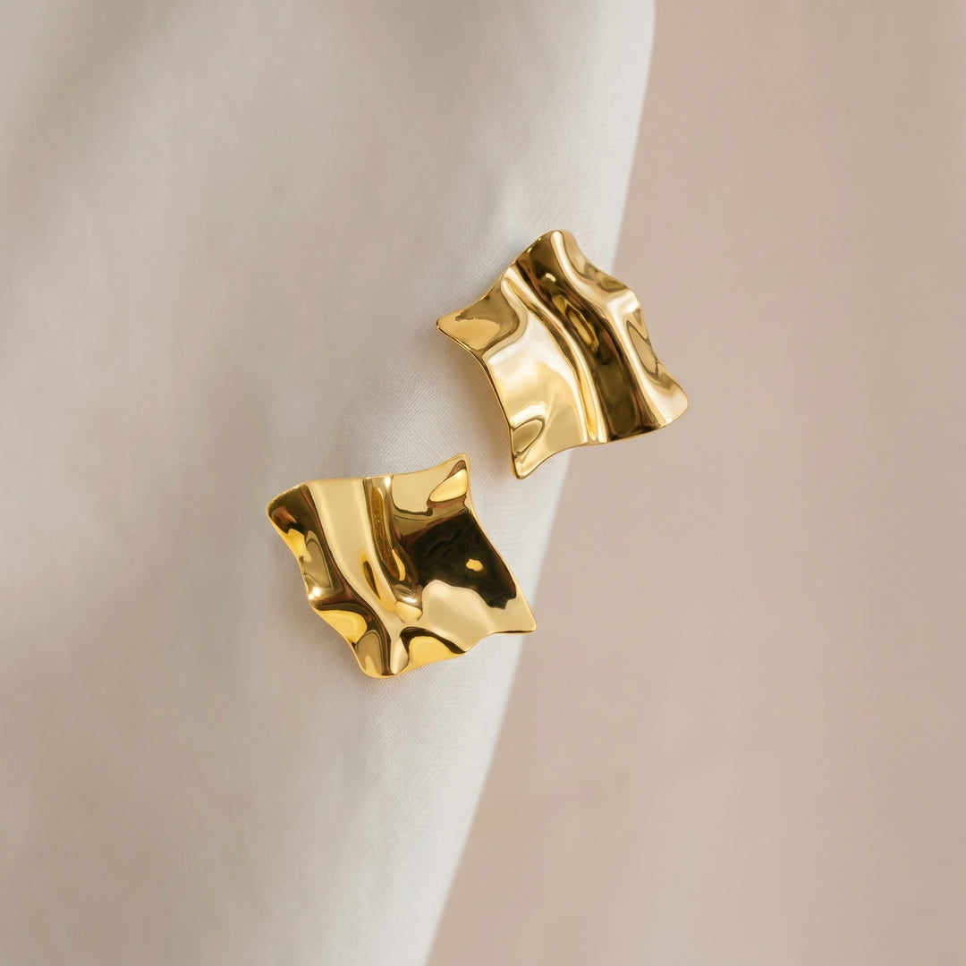 Gold earrings on a white surface with a neutral background