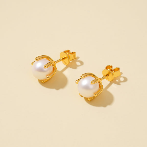 Gold earrings with pearl-like stones on a beige background